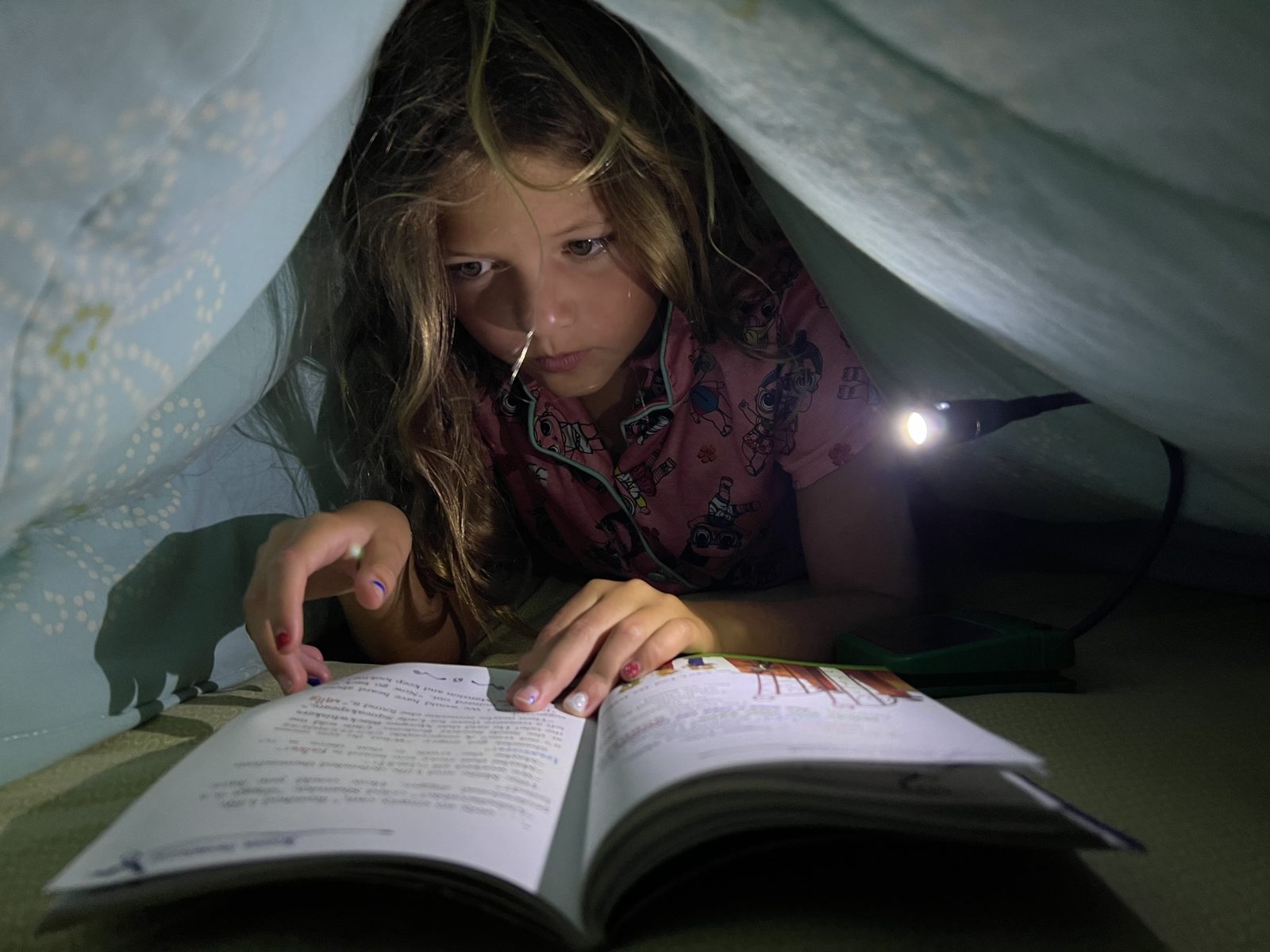 Girl reading under a blanket fort with a Luke Light