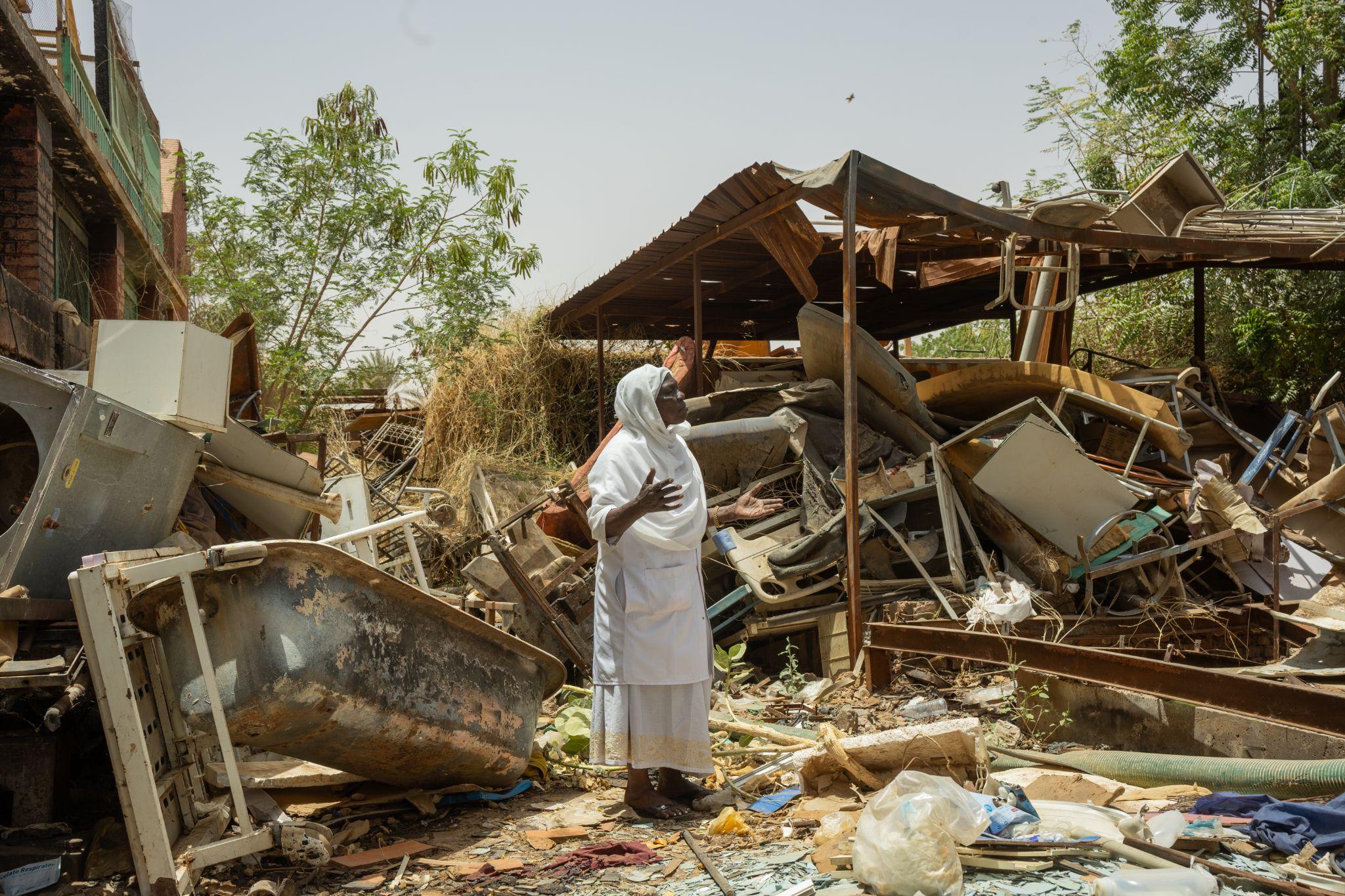 A woman in white stands among the wreckage of a damaged hospital in Sudan